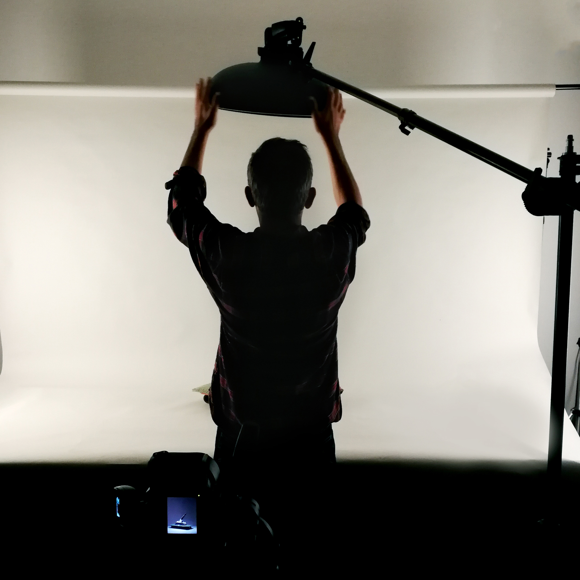 Reproduction of Artworks Photographer adjusting studio lighting to reproduce a small object against a white backdrop